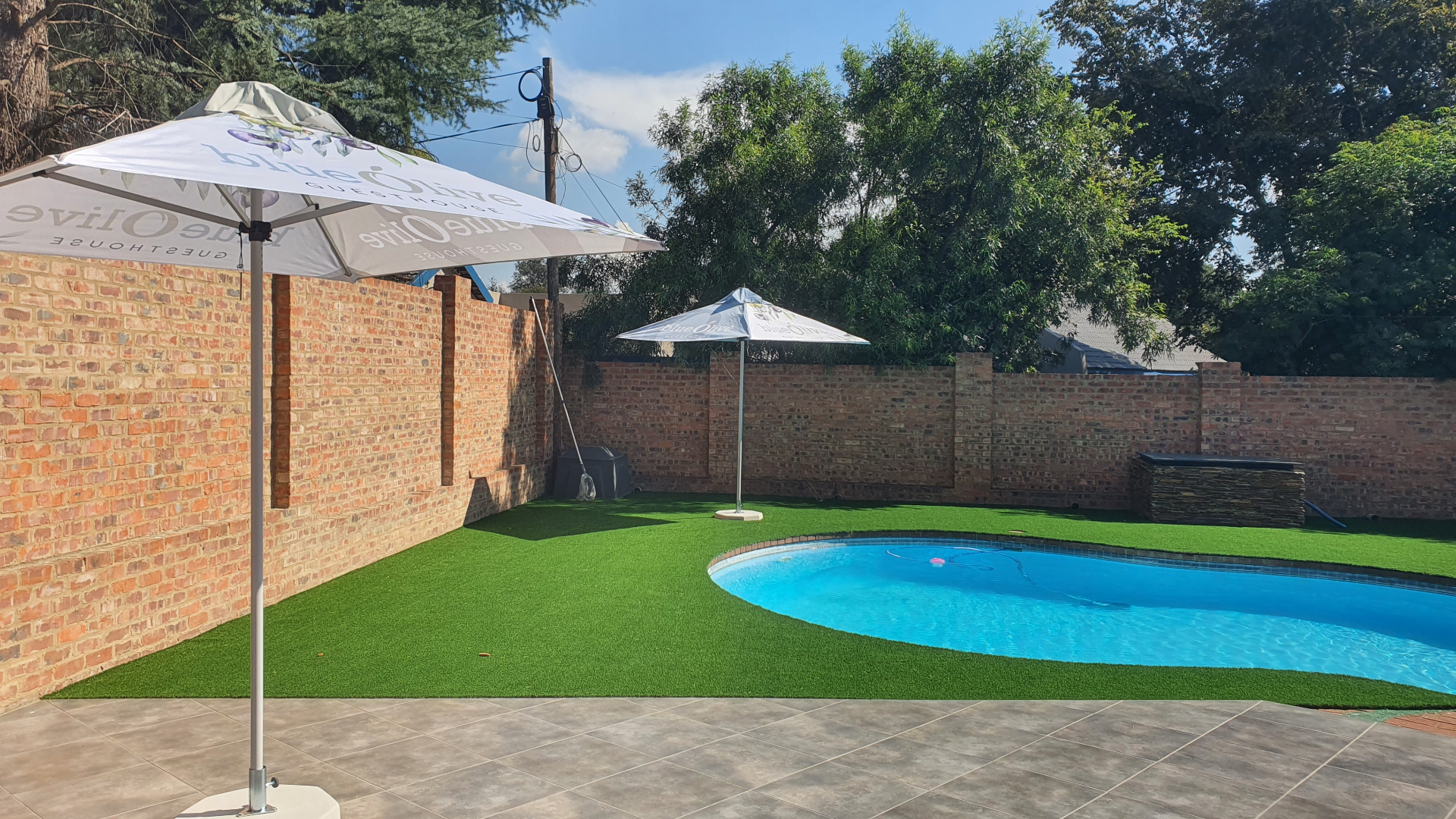 Swimming pool with umbrellas and green lawn surrounded by brick walls